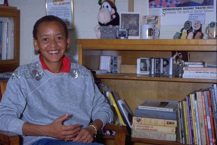 Nikki Giovanni in her office surrounded by books and smiling
