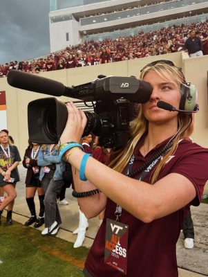 student holding large video camera on football field sidelines