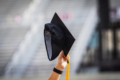 Graduate holding a graduation cap up in the air.