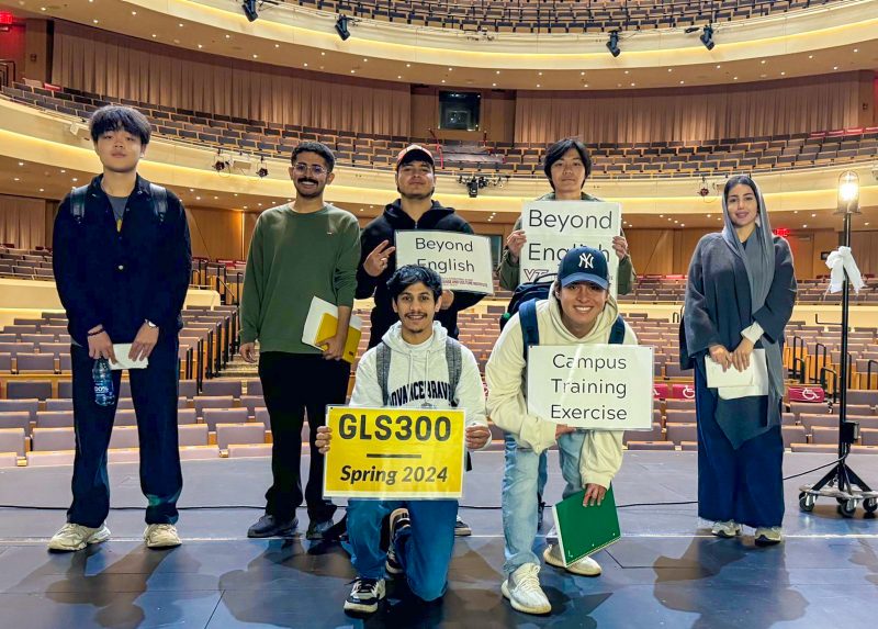 Seven students pose with signs about CTX while standing on the stage at Moss Arts